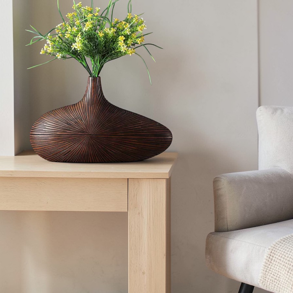 Dark round wooden vase styled with flowers beside chair