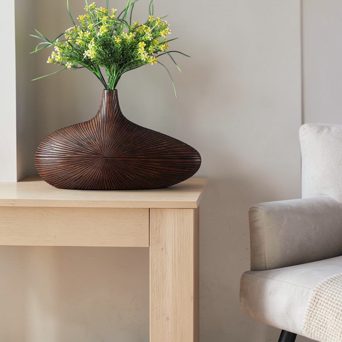 Dark round wooden vase styled with flowers beside chair